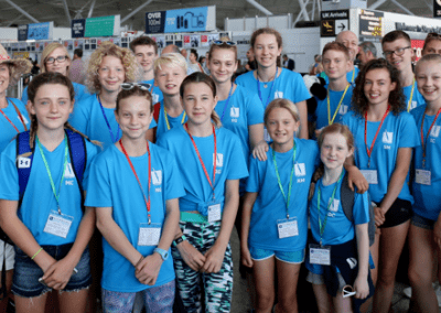 A large group of around Cambridge Dive Team divers assembled at an airport. All the divers are wearing light blue CDT tee-shirts and the majority are children.