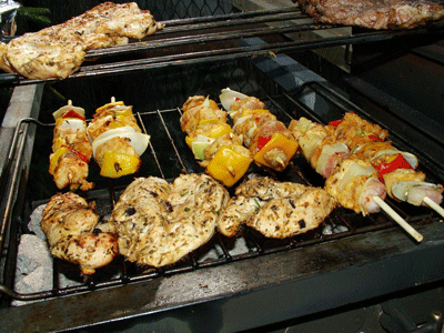 Close up of a barbecue grill which has chicken breasts and skewered meat on it.