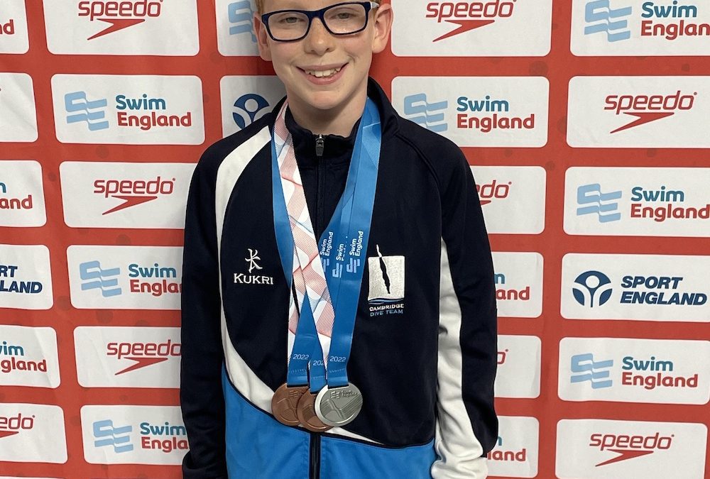 Rufus sporting three medals and standing in front of a board covered in sponsorship logos.