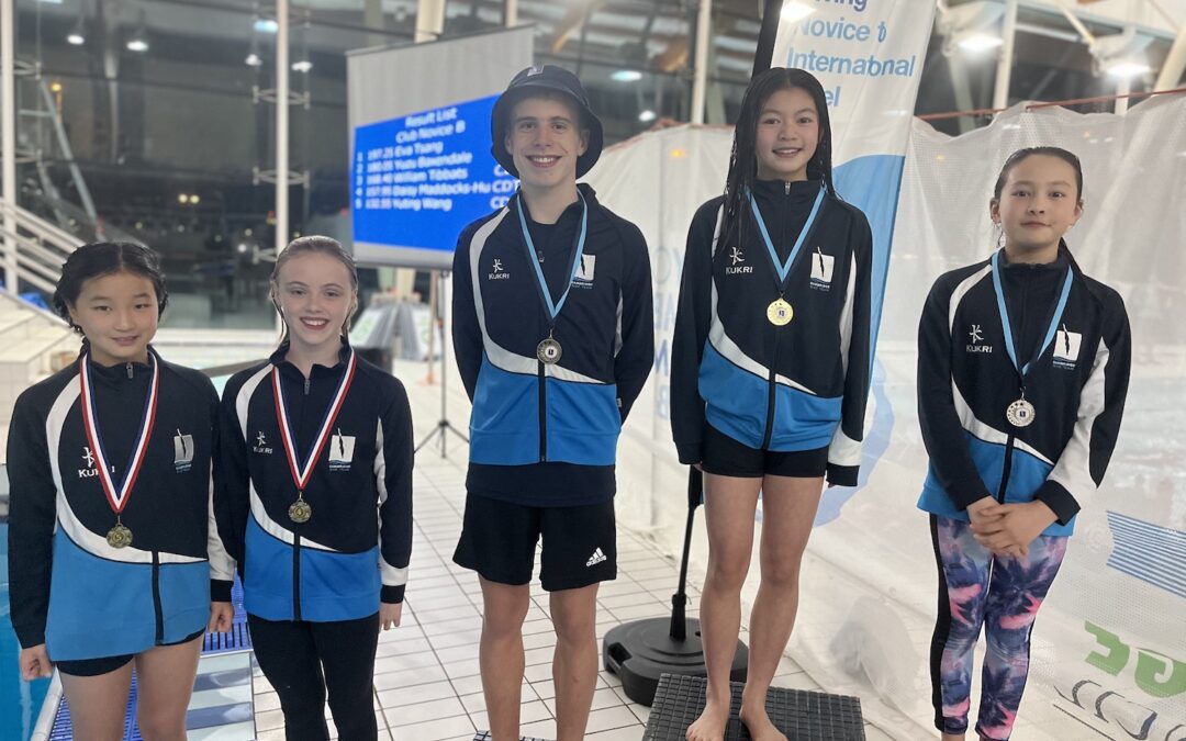 Five young novice divers standing on a podium on poolside.