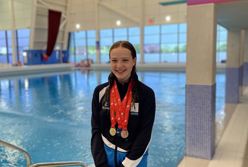 Young CDT diver standing on poolside and wearing three medals around her neck